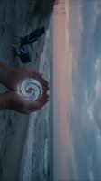 Hands holding glowing spiral energy orb at ocean beach during sunset with dramatic sky and waves for spiritual meditation and healing concepts.