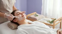 Young Asian woman receiving professional facial treatment with white cream mask at luxury spa salon for skincare and wellness relaxation therapy.