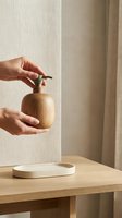 Hands using wooden soap dispenser pump bottle in minimalist bathroom interior with natural beige tones and soft lighting for sustainable living.