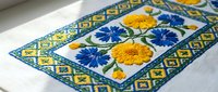 Embroidered floral table runner with blue cornflowers and yellow marigolds in traditional folk art style on white linen fabric for home decor.