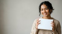 Young woman with dark wavy hair and South Asian ethnicity holding blank white tablet device, wearing beige cardigan, smiling at camera against neutral background for app or product display.