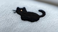 Black cat silhouette embroidered on white fabric with delicate stitching detail and curved tail design, featuring minimalist style and golden eye accent.