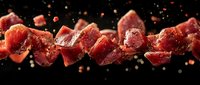 Fresh raw beef cubes flying in air with spices on black background, showcasing premium meat for culinary use.