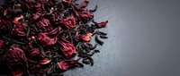 Dried hibiscus flowers and black tea leaves mixed together on gray surface for herbal beverage preparation.