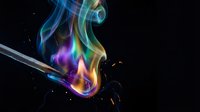 Colorful rainbow smoke flames rising from metal lighter creating vibrant blue green purple yellow swirls against black background for creative designs.