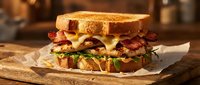 Gourmet bacon cheeseburger with melted cheese and fresh lettuce on toasted bread, served on rustic wooden board in warm kitchen setting for food photography.