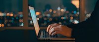 Professional working late on laptop with city lights bokeh background for business and technology concepts.