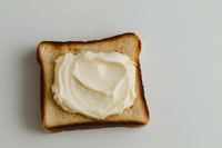 Fresh slice of toasted white bread with creamy butter spread in heart shape on light gray background, minimalist food photography composition.