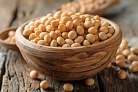 Raw soybeans in wooden bowl on rustic table, close up view of yellow dried legumes. Natural protein source for healthy vegetarian nutrition.