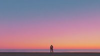 Romantic couple silhouette embracing on beach during stunning sunset with colorful sky gradient from purple to orange over calm ocean horizon.