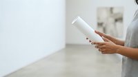 Woman holding blank white cylindrical product container in modern interior space for branding and packaging mockup purposes.