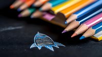 Colorful wooden pencils arranged on dark background with creative chalk drawing of fish. Artistic composition showing creativity and education concept.