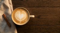 Coffee cup with heart latte art on rustic wooden table with cinnamon stick and linen napkin for cafe menu design and morning beverage concepts.
