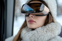 Young woman wearing futuristic VR glasses and winter clothing with beanie hat and fur collar, side view portrait against blurred snowy background.