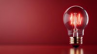 Glowing vintage light bulb with illuminated filament on dark red background, dramatic lighting creates atmospheric mood for creative and innovation concepts.