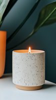 Minimalist speckled ceramic candle holder with burning flame against dark green background, featuring natural plant elements and modern design aesthetic.