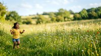 Young child in yellow shirt running through wildflower meadow on sunny day, enjoying outdoor nature play and freedom in countryside landscape.