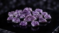 Purple amethyst crystal cluster gemstones on dark reflective surface for jewelry making, healing practices, and mineral collection displays.