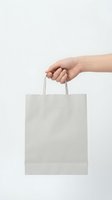 Hand holding blank white paper shopping bag on neutral background for retail branding mockup and commercial presentation design projects.