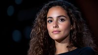 Young woman with curly brown hair and natural makeup against dark background, illuminated by dramatic lighting for portrait photography.
