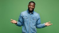 Confident African American man in denim jacket gesturing with open arms against green background, expressing welcome or presentation for business or lifestyle content.