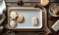 Homemade sugar cookies with white icing on ceramic plate, star anise and burning candle on rustic wooden table. Winter holiday baking atmosphere.