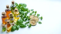 Natural essential oil bottles with fresh herbs basil oregano and dried citrus slices on white background for aromatherapy wellness spa treatments.