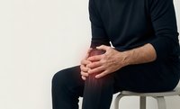 Man in black casual wear sitting on white chair with hands clasped, isolated on light background for modern lifestyle and business concepts.