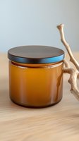 Amber glass jar with black metal lid on wooden surface next to decorative branch, minimalist composition for cosmetic and wellness product photography.