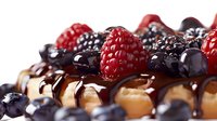 Fresh raspberries and blueberries on golden waffle drizzled with dark chocolate sauce, extreme close up macro food photography with selective focus.