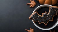 Halloween bat-shaped gingerbread cookie floating in coffee cup with star anise spices on dark background for autumn seasonal treats and festive beverages.