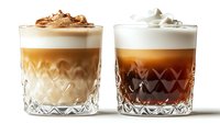 Two layered coffee cocktails in crystal cut glasses with whipped cream toppings on white background. Left glass features light caramel layers, right glass shows dark espresso layers. Isolated beverages ready for menu design, advertising, and hospitality marketing.