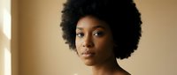 Young African American woman with natural afro hairstyle looking confidently at camera in warm indoor lighting for beauty and lifestyle concepts.