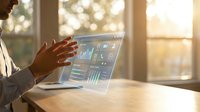 Young male professional in business attire analyzing financial data and analytics on laptop screen with holographic display overlay in bright office environment with natural sunlight.