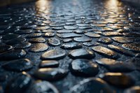 Wet cobblestone street surface with golden light reflections at night creates dramatic urban texture and atmosphere for background or architectural design projects.
