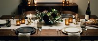 Elegant dinner table setting with dark plates, white napkins, fresh greenery centerpiece, candlelight, and wine for formal dining occasions and event planning.