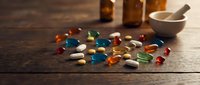 Colorful pharmaceutical pills and capsules scattered on wooden table with medicine bottles and mortar pestle in background for healthcare concepts.