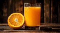 Fresh orange juice in glass with sliced orange half on rustic wooden table. Healthy breakfast drink, vitamin C rich citrus beverage for morning nutrition.