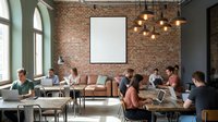 Modern coworking space with diverse professionals working at laptops in industrial loft office featuring exposed brick walls and blank presentation screen.