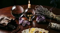 Mystical fortune telling setup with crystal balls, tarot cards, amethyst crystals, candle, lavender, and sage on a dark wooden table.