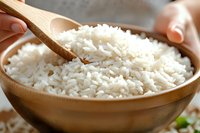 Steamed white rice served in wooden bowl with bamboo spoon, close up view showing fluffy texture and individual grains. Fresh cooked Asian cuisine staple.