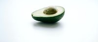 Fresh ripe avocado half with pit on clean white background isolated for healthy cooking and nutrition design projects.