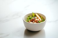 Fresh mixed salad with grilled chicken, nuts and greens served in white ceramic bowl on marble background, healthy lunch concept.