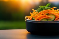 Fresh carrot and cucumber julienne salad with mint garnish in dark bowl on wooden table during golden hour sunset lighting for healthy eating concepts.