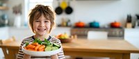 Happy young boy holding fresh vegetables in modern kitchen, promoting healthy eating habits and family cooking activities.