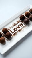 Chocolate truffles dusted with cocoa powder arranged on a white plate with the word Love stenciled in cocoa, perfect for Valentine's Day.