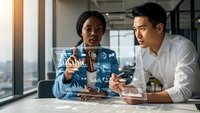 African American businesswoman and Asian businessman analyzing holographic data interface in modern office environment for technology collaboration.