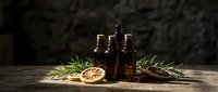 Dark amber essential oil bottles with dried orange slices and rosemary sprigs on rustic wooden surface for natural aromatherapy and wellness treatments.