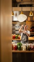 Professional male chef tossing pizza dough in modern restaurant kitchen with brick oven and pendant lighting for culinary business and food service industry.