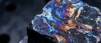 Iridescent mineral specimen displaying vibrant blue, purple and copper colors with metallic luster on dark crystalline surface for geology education.